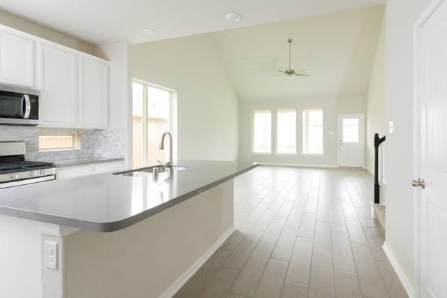 5018 Brewcastle Ln, Katy, TX 77493 - kitchen with stainless steel microwave, range, a center island with sink, decorative backsplash, and light wood-type flooring