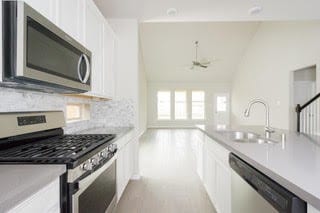 5018 Brewcastle Ln, Katy, TX 77493 - kitchen featuring stainless steel appliances, white cabinets, tasteful backsplash, light countertops, and vaulted ceiling
