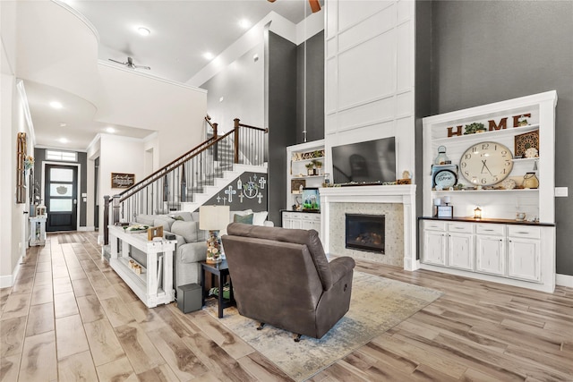 4802 Wagtail Way Ln, League City, TX 77573 - living room featuring light wood finished floors, a towering ceiling, stairs, a tiled fireplace, and crown molding