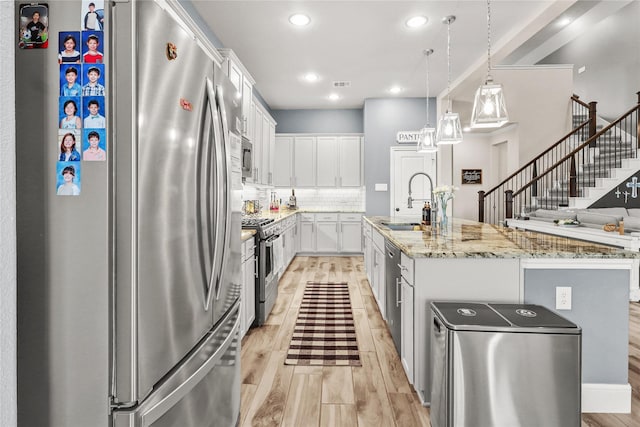 4802 Wagtail Way Ln, League City, TX 77573 - kitchen featuring appliances with stainless steel finishes, light wood-style floors, decorative backsplash, white cabinetry, and an island with sink