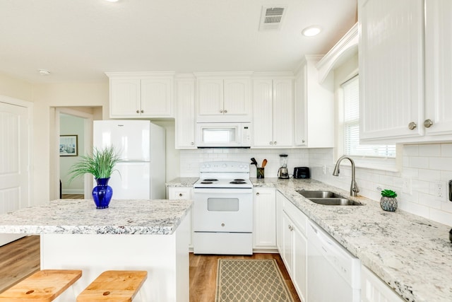1214 Fort Velasco Dr, Surfside Beach, TX 77541 - kitchen with white appliances, wood finished floors, a kitchen bar, white cabinets, and decorative backsplash