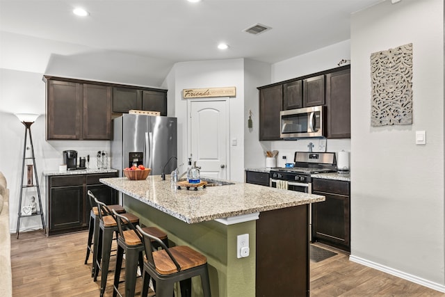 20214 Portbec Dr, New Caney, TX 77357 - kitchen with appliances with stainless steel finishes, a breakfast bar, light wood-type flooring, dark brown cabinetry, and an island with sink