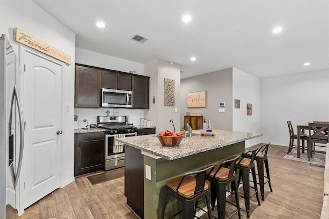 20214 Portbec Dr, New Caney, TX 77357 - kitchen with appliances with stainless steel finishes, a kitchen breakfast bar, a kitchen island with sink, light wood-style flooring, and light stone counters
