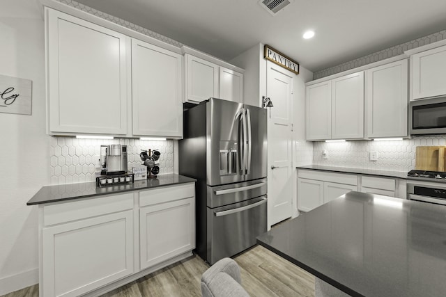 10009 Gray Jay Ct, Conroe, TX 77384 - kitchen with appliances with stainless steel finishes, dark countertops, decorative backsplash, light wood-style flooring, and recessed lighting