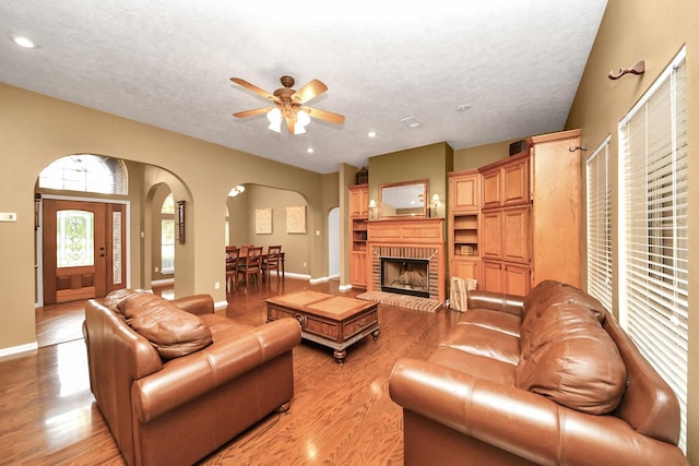 5874 Natchez Trce, Baytown, TX 77523 - living room with arched walkways, light wood-style flooring, a ceiling fan, a textured ceiling, and a brick fireplace