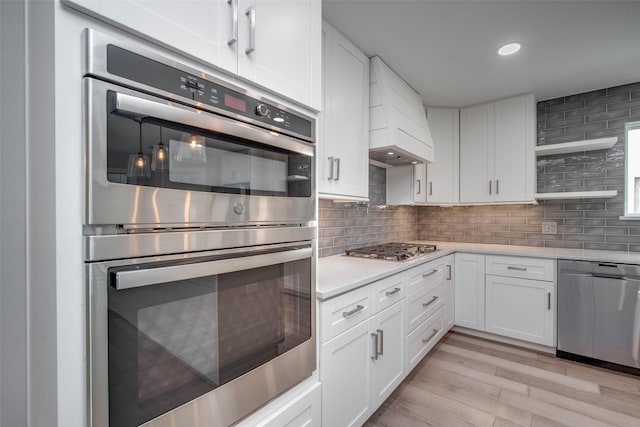 7710 Meadowvale Dr, Houston, TX 77063 - kitchen with stainless steel appliances, light countertops, white cabinetry, light wood-type flooring, and backsplash