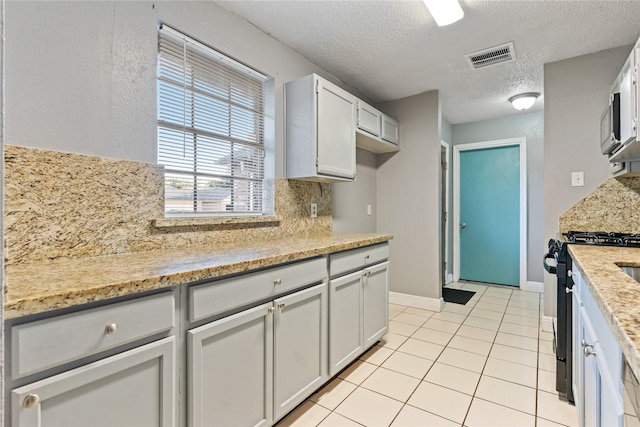 20062 S Pecos Valley Trl, Katy, TX 77449 - kitchen featuring gas range, a textured ceiling, backsplash, light tile patterned flooring, and light stone countertops