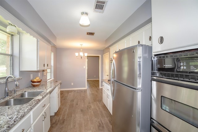 13329 24th St, Santa Fe, TX 77510 - kitchen with appliances with stainless steel finishes, white cabinets, a chandelier, light wood-style flooring, and light stone countertops