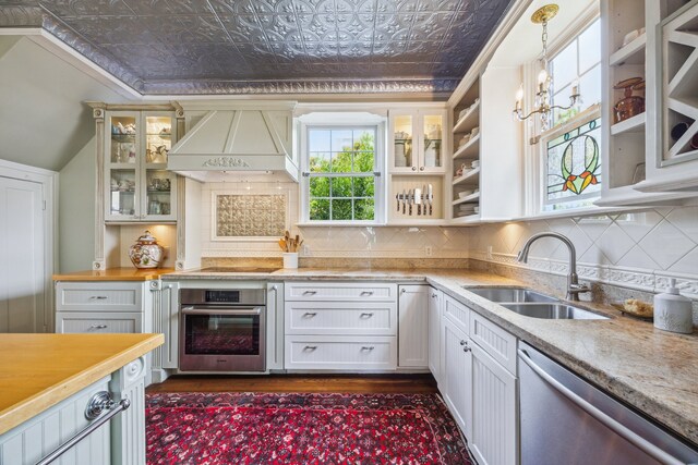607 11th St, Galveston, TX 77550 - kitchen featuring appliances with stainless steel finishes, custom exhaust hood, an ornate ceiling, tasteful backsplash, and glass insert cabinets