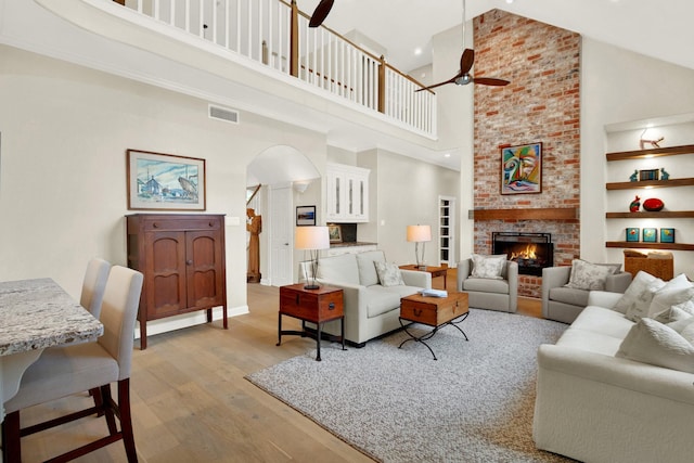 13718 Gainesway Dr, Cypress, TX 77429 - living area featuring high vaulted ceiling, a ceiling fan, arched walkways, light wood-style floors, and a brick fireplace