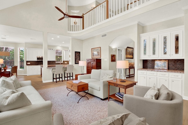 13718 Gainesway Dr, Cypress, TX 77429 - living room featuring a ceiling fan, arched walkways, a high ceiling, light wood-style flooring, and ornamental molding