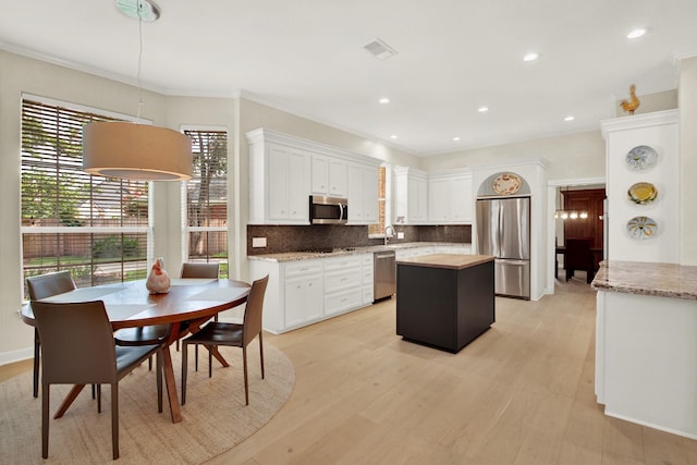 13718 Gainesway Dr, Cypress, TX 77429 - kitchen featuring appliances with stainless steel finishes, a center island, white cabinetry, decorative backsplash, and light wood-style floors