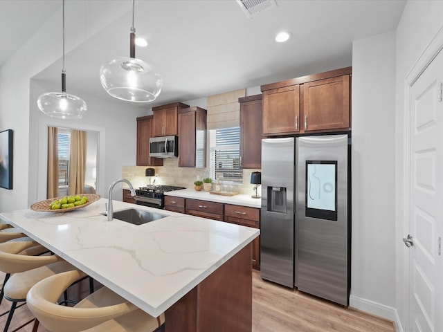 9217 Washington Hts, Houston, TX 77063 - kitchen featuring stainless steel appliances, tasteful backsplash, light wood finished floors, a center island with sink, and a kitchen breakfast bar