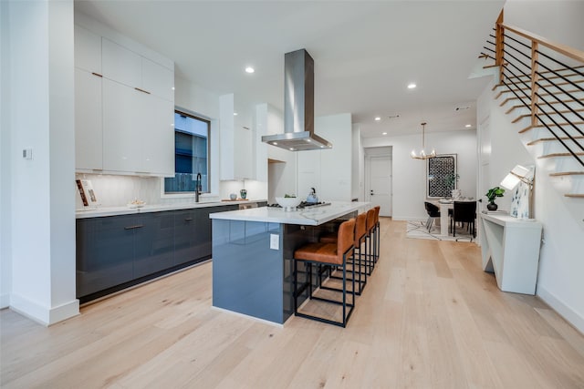1937 W Clay St, Houston, TX 77019 - kitchen featuring wall chimney exhaust hood, modern cabinets, a kitchen bar, light wood-style flooring, and a kitchen island