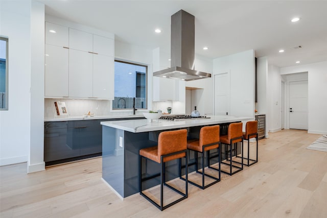 1937 W Clay St, Houston, TX 77019 - kitchen with island range hood, modern cabinets, light wood-type flooring, light countertops, and white cabinets