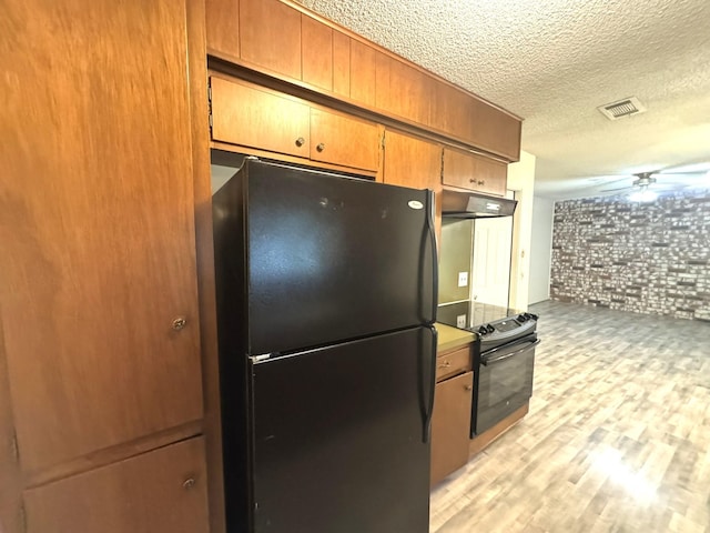 1722 Briar Ln, Wharton, TX 77488 - kitchen with black appliances, under cabinet range hood, brick wall, a textured ceiling, and light wood-type flooring