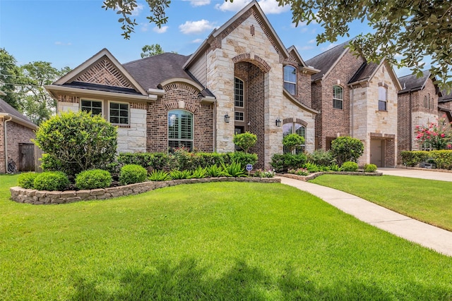 5434 Lockwood Bend Ln, Sugar Land, TX 77479 - french country inspired facade with stone siding, a front lawn, brick siding, and roof with shingles