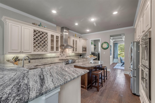 5434 Lockwood Bend Ln, Sugar Land, TX 77479 - kitchen featuring wall chimney range hood, appliances with stainless steel finishes, a kitchen island, backsplash, and light stone countertops