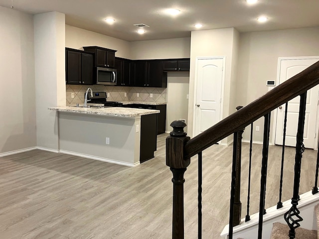 15806 Perthshire Creek Dr, Humble, TX 77346 - kitchen with appliances with stainless steel finishes, dark cabinets, light wood-type flooring, decorative backsplash, and a peninsula