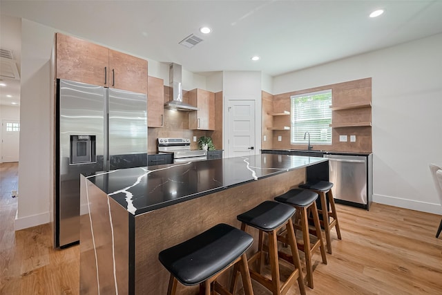2015 Creston Dr, Houston, TX 77026 - kitchen featuring wall chimney exhaust hood, appliances with stainless steel finishes, open shelves, light wood-style floors, and tasteful backsplash