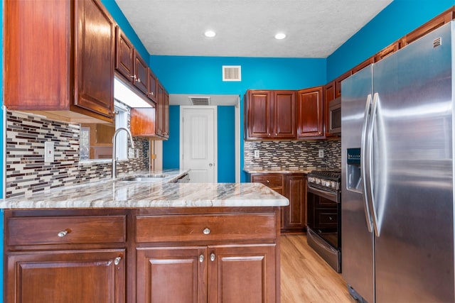 5602 Society Ln, Houston, TX 77084 - kitchen with appliances with stainless steel finishes, light wood finished floors, light stone counters, backsplash, and a peninsula