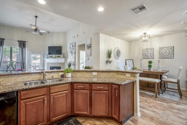 18605 Syndee Loch Ct, Spring, TX 77379 - kitchen with black dishwasher, a ceiling fan, light stone counters, light wood-style floors, and a tiled fireplace