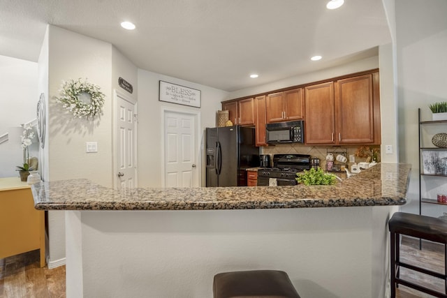 18605 Syndee Loch Ct, Spring, TX 77379 - kitchen with brown cabinets, black appliances, dark stone countertops, a kitchen bar, and recessed lighting