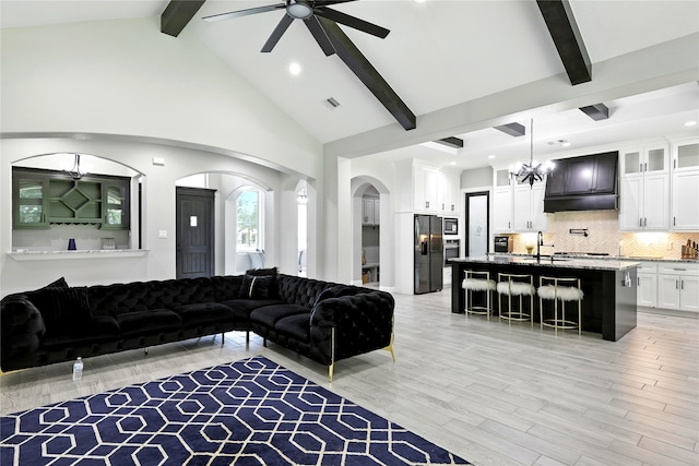 17114 Leon Ct, Splendora, TX 77372 - living area featuring a chandelier, ceiling fan, beamed ceiling, arched walkways, and light wood-type flooring