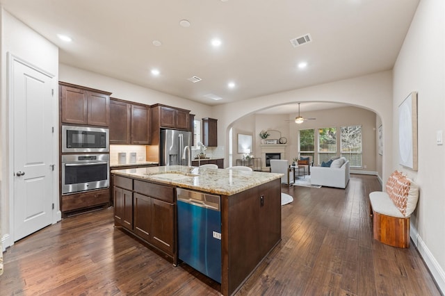 13207 Parkway Meadows Dr, Houston, TX 77077 - kitchen with stainless steel appliances, arched walkways, a fireplace, open floor plan, and dark brown cabinetry