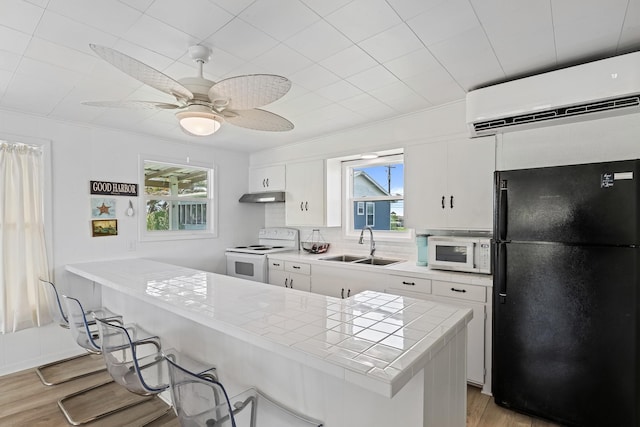 106 E Madison Ave, Port O Connor, TX 77982 - kitchen featuring white appliances, an AC wall unit, under cabinet range hood, tile counters, and light wood finished floors