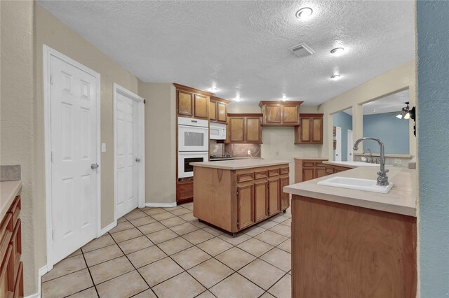 10802 4th 1/2 St, Santa Fe, TX 77510 - kitchen with white appliances, a textured ceiling, light countertops, brown cabinets, and light tile patterned floors