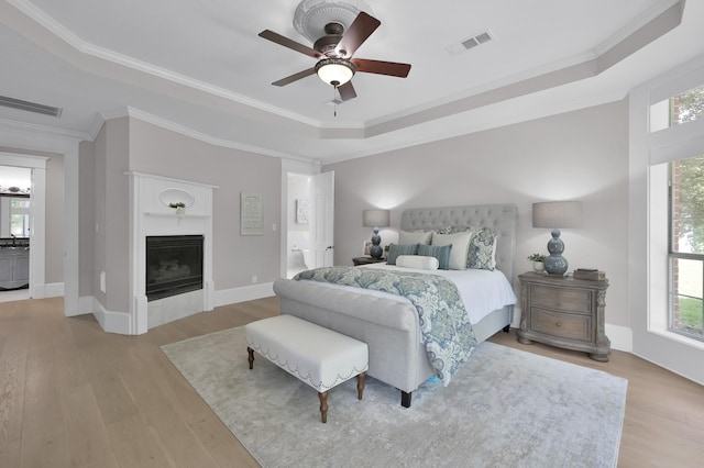 15203 Wildwood Cir, Magnolia, TX 77354 - bedroom featuring a raised ceiling, light wood finished floors, ornamental molding, a fireplace, and ceiling fan