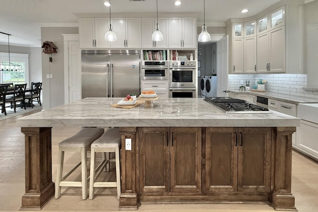 15203 Wildwood Cir, Magnolia, TX 77354 - kitchen with stainless steel appliances, ornamental molding, backsplash, washer and clothes dryer, and white cabinets