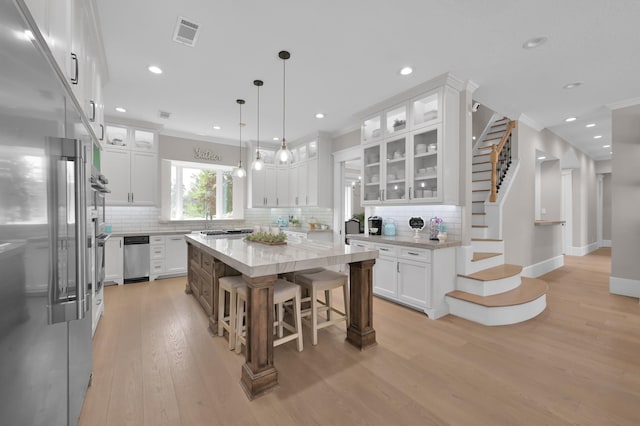 15203 Wildwood Cir, Magnolia, TX 77354 - kitchen featuring appliances with stainless steel finishes, light wood finished floors, white cabinets, backsplash, and ornamental molding