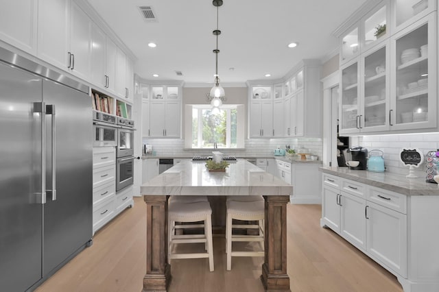15203 Wildwood Cir, Magnolia, TX 77354 - kitchen featuring appliances with stainless steel finishes, white cabinetry, light wood-type flooring, tasteful backsplash, and crown molding