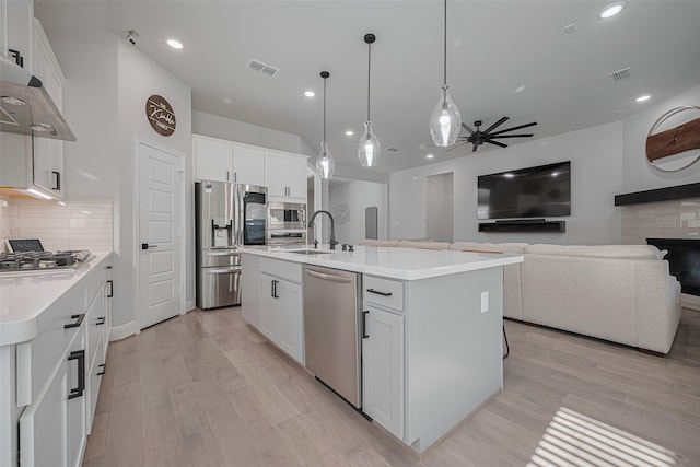 30706 Southern Dewberry Ct, Fulshear, TX 77441 - kitchen featuring appliances with stainless steel finishes, ceiling fan, wall chimney exhaust hood, backsplash, and light wood finished floors