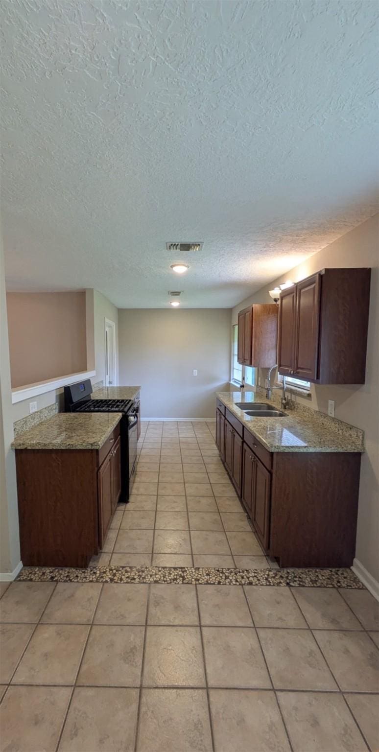 1305 Serpentine Dr, Houston, TX 77029 - kitchen with gas stove, a textured ceiling, light tile patterned floors, and light stone counters