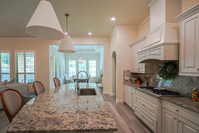 13114 Sierra National Dr, Humble, TX 77346 - kitchen with stainless steel gas stovetop, light wood-type flooring, premium range hood, tasteful backsplash, and crown molding