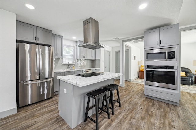 8218 Waynemer Way, Houston, TX 77040 - kitchen featuring appliances with stainless steel finishes, gray cabinetry, island exhaust hood, dark wood finished floors, and a breakfast bar area