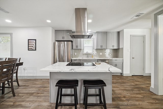 8218 Waynemer Way, Houston, TX 77040 - kitchen with island exhaust hood, appliances with stainless steel finishes, gray cabinets, a kitchen breakfast bar, and dark wood-type flooring