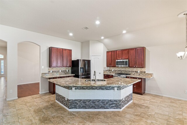 15218 Zenith Glen Ln, Cypress, TX 77429 - kitchen featuring appliances with stainless steel finishes, tasteful backsplash, a kitchen island with sink, arched walkways, and light stone countertops