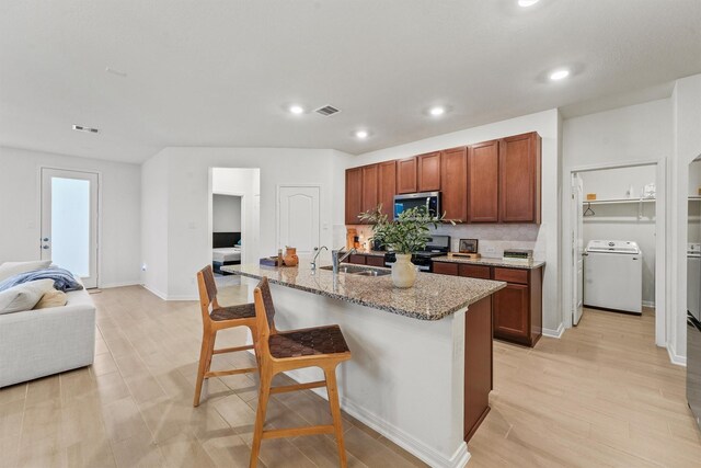 7003 Tehama Ln, Rosharon, TX 77583 - kitchen featuring stainless steel microwave, washer / clothes dryer, electric range, a breakfast bar area, and light stone countertops