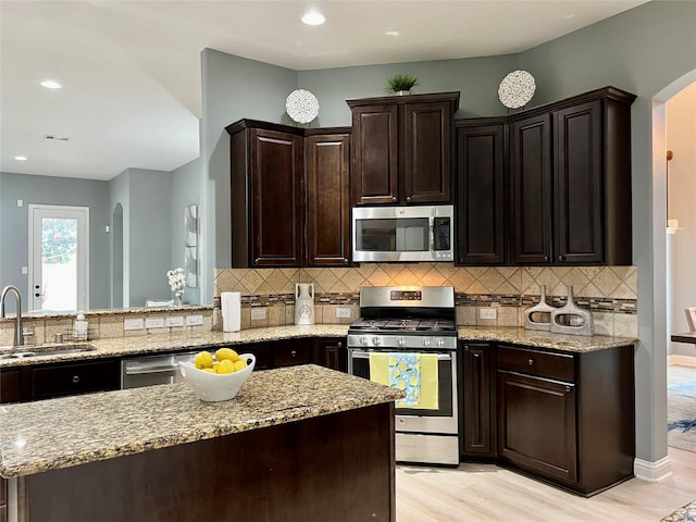 18718 Fairmont Springs Ct, Cypress, TX 77429 - kitchen featuring stainless steel appliances, arched walkways, light stone counters, light wood-type flooring, and tasteful backsplash