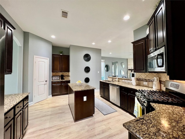 18718 Fairmont Springs Ct, Cypress, TX 77429 - kitchen featuring appliances with stainless steel finishes, a peninsula, backsplash, light wood finished floors, and light stone countertops