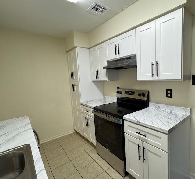9001 Imogene St Unit A, Houston, TX 77036 - kitchen with under cabinet range hood, stainless steel electric stove, white cabinetry, light stone countertops, and light tile patterned floors