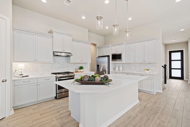 1919 Waters Branch Dr, Missouri City, TX 77459 - kitchen featuring appliances with stainless steel finishes, under cabinet range hood, light countertops, decorative backsplash, and a center island with sink