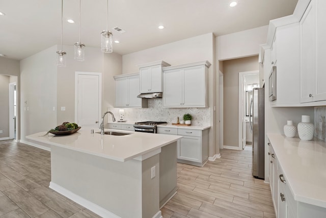 1919 Waters Branch Dr, Missouri City, TX 77459 - kitchen with under cabinet range hood, tasteful backsplash, stainless steel appliances, wood tiled floors, and a kitchen island with sink
