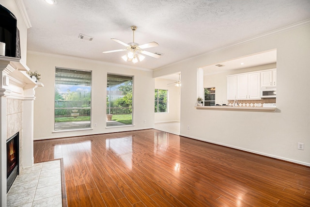 1726 Roaring Springs Ln, Seabrook, TX 77586 - unfurnished living room with a ceiling fan, a tile fireplace, light wood-style flooring, ornamental molding, and a textured ceiling