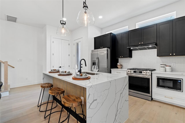 4110 Cortlandt St, Houston, TX 77018 - kitchen with stainless steel appliances, under cabinet range hood, dark cabinetry, light wood-style flooring, and backsplash