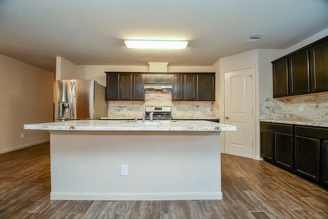 2026 Naplechase Crest Dr, Spring, TX 77373 - kitchen featuring appliances with stainless steel finishes, dark wood-type flooring, decorative backsplash, a kitchen island with sink, and dark brown cabinets